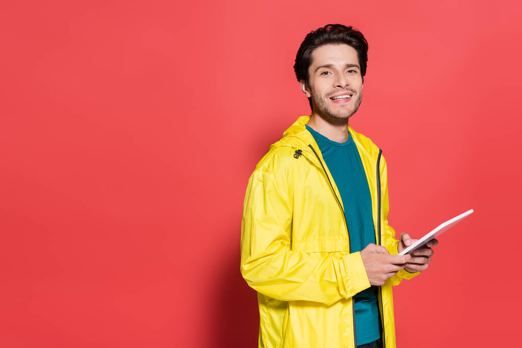Sportsman holding digital tablet and smiling at camera on red background  - Foto, immagini