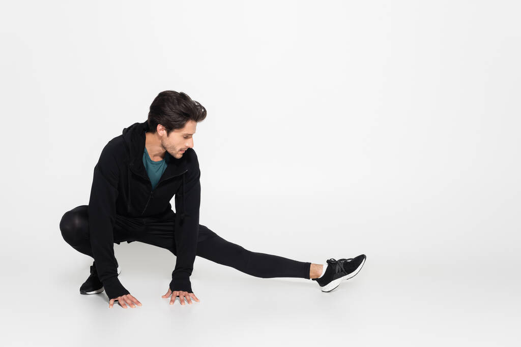 Brunette sportman stretching op grijze achtergrond  - Foto, afbeelding