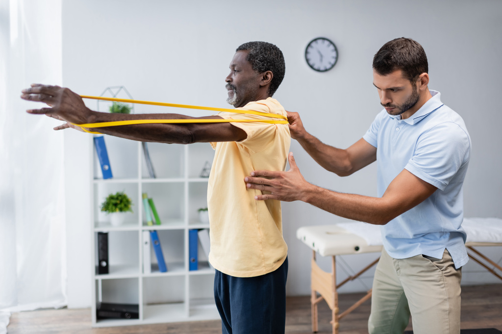 young physical therapist assisting mature african american man training with elastics - Photo, Image