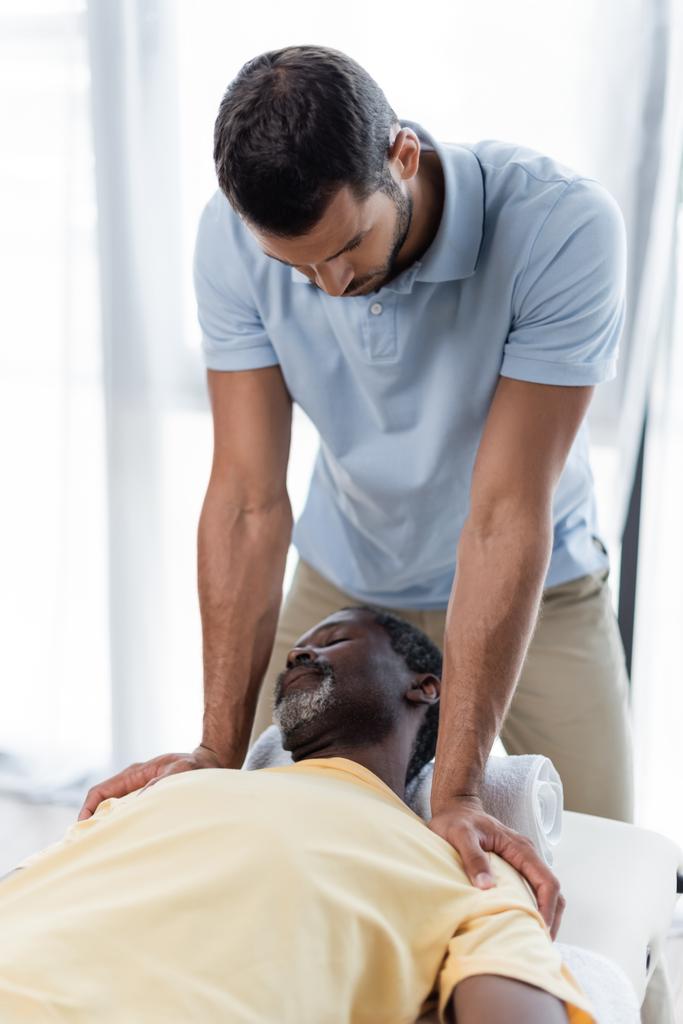 homem americano africano maduro deitado na mesa de massagem durante o tratamento de reabilitação - Foto, Imagem