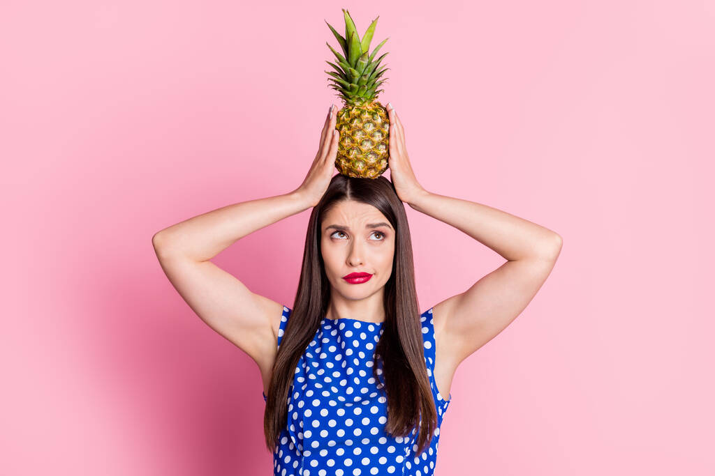 Фото молодої жінки тримає ананас на голові нещасливо думають, що виглядає екзотична фруктова їжа ізольована на фоні рожевого кольору
 - Фото, зображення