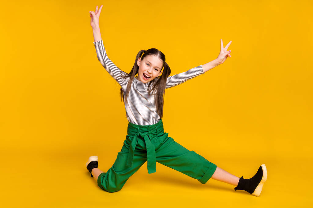 Pleine photo du corps de la jeune fille heureux sourire positif acrobaties flexible montrer la paix cool v-signe isolé sur fond de couleur jaune - Photo, image