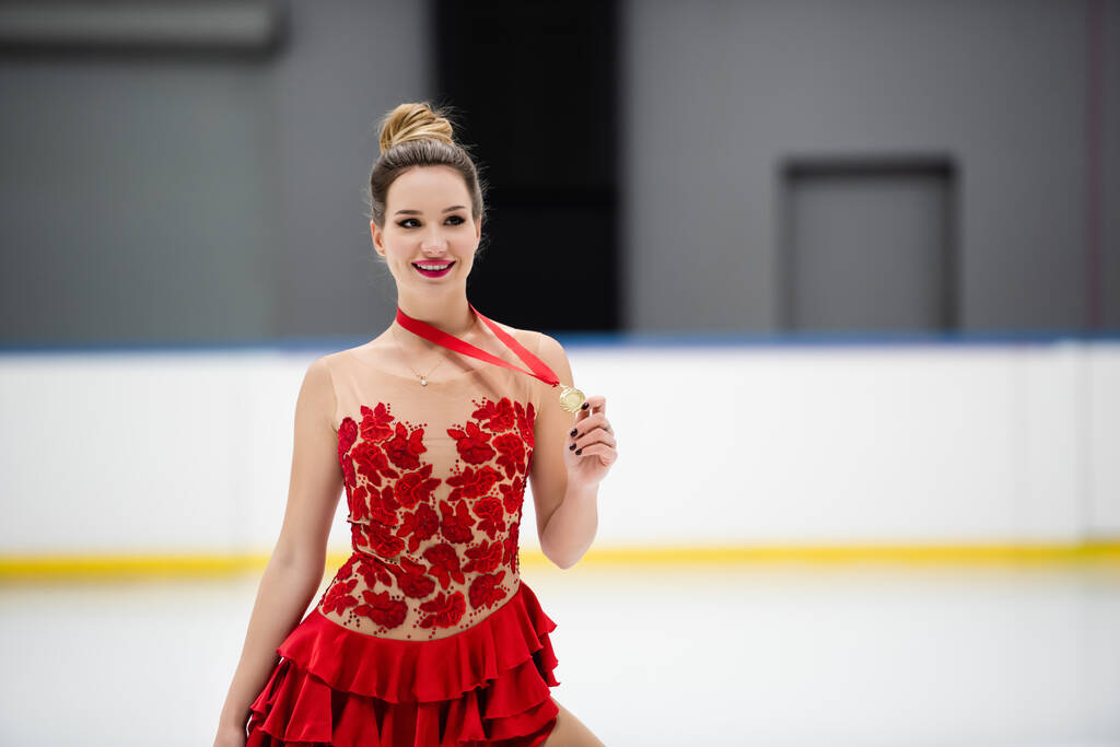 happy figure skater in red dress holding golden medal  - Foto, Bild