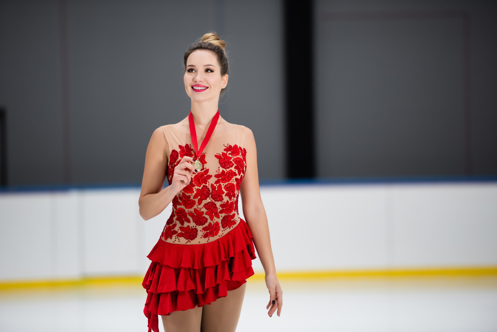 smiling figure skater in red dress holding golden medal on ice arena - Photo, Image