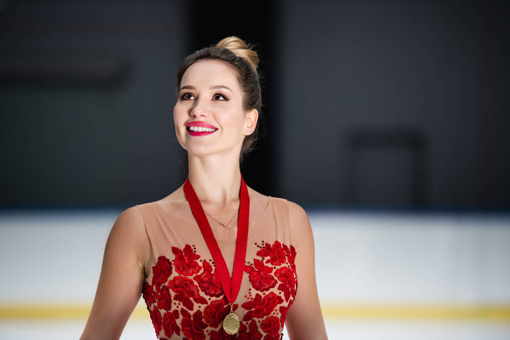 Glückliche Eiskunstläuferin in rotem Kleid und Schleife mit Goldmedaille  - Foto, Bild