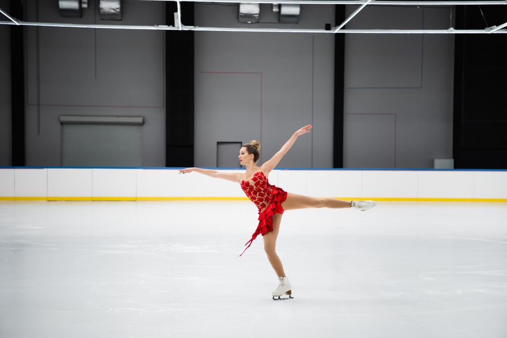 pełna długość łyżwiarz figurowy w czerwonej sukience wykonywania wielbłąda spin w profesjonalnej arenie lodowej - Zdjęcie, obraz