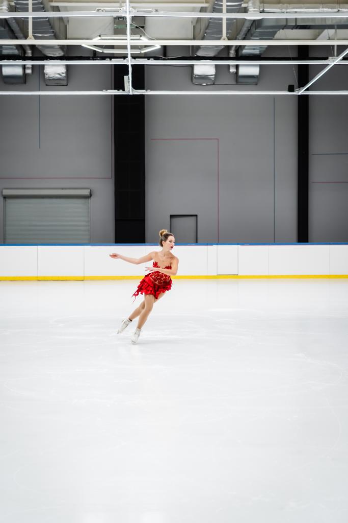 Profesyonel buz arenasında kırmızı elbiseli bir kadın buz pateni yapıyor. - Fotoğraf, Görsel