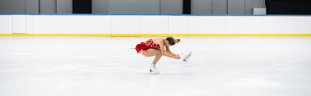 full length of young woman in dress performing sit spin in professional ice arena, banner - Foto, Bild