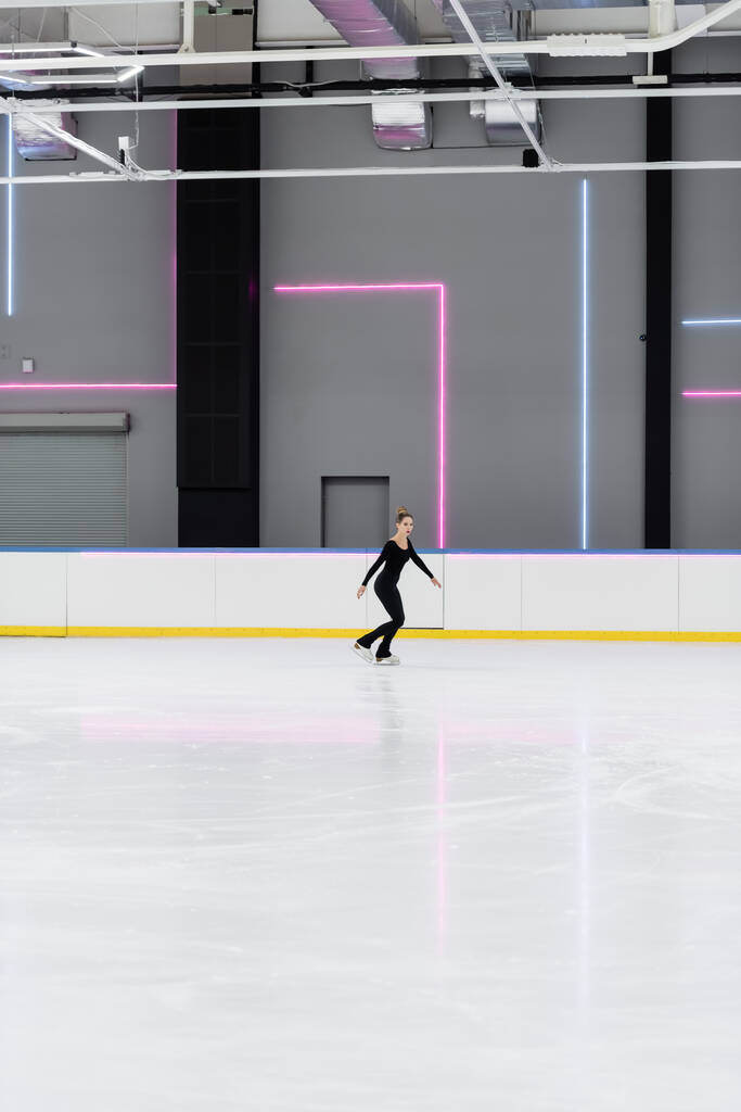 Profesyonel buz arenasında buz pateni yapan siyah elbiseli artistik patinajcı. - Fotoğraf, Görsel