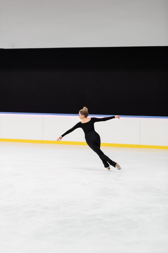 Eiskunstläufer in voller Länge im schwarzen Body mit ausgestreckten Händen in der Eisarena - Foto, Bild