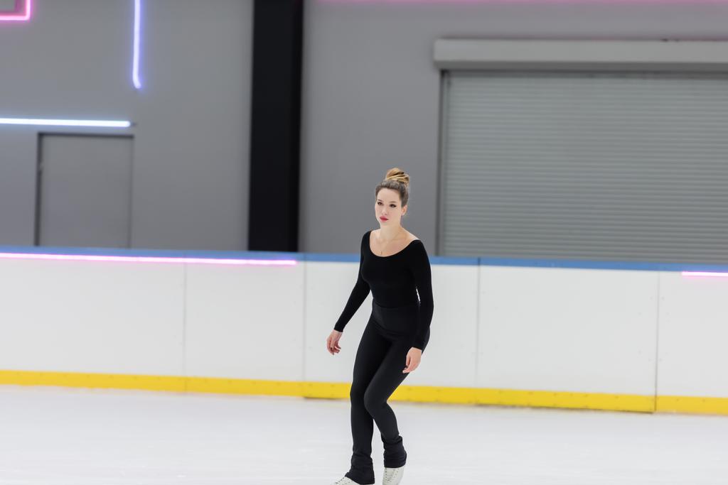 Junge Eiskunstläuferin in schwarzem Body läuft in Eissporthalle - Foto, Bild