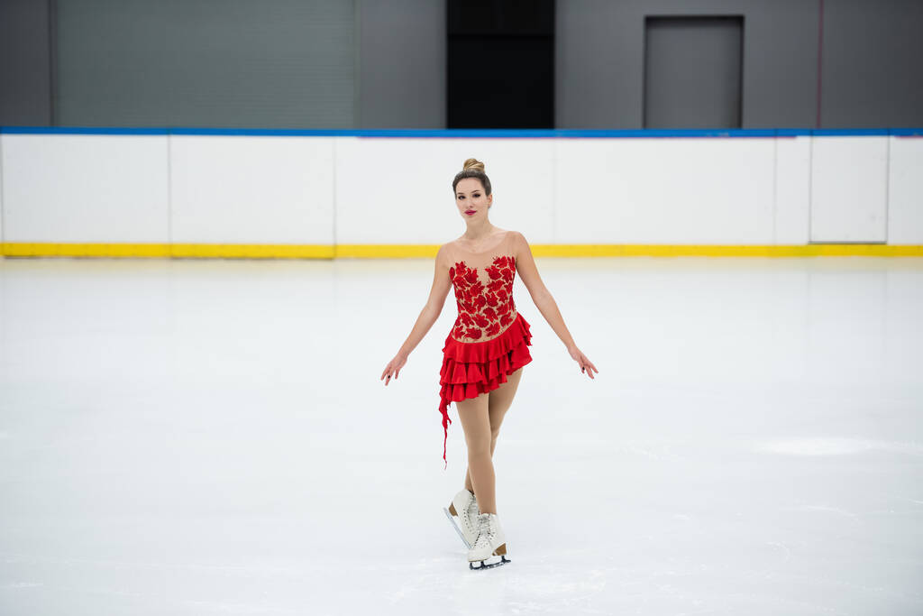 pełna długość młodej kobiety w czerwonej sukience łyżwiarstwo figurowe w profesjonalnym lodowisku - Zdjęcie, obraz