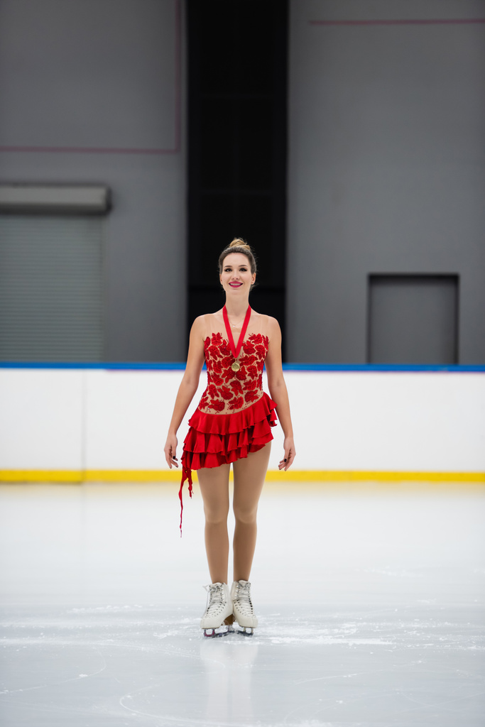 pełna długość wesoły łyżwiarz figurowy w czerwonej sukience ze złotym medalem łyżwiarstwo na lodowisku - Zdjęcie, obraz