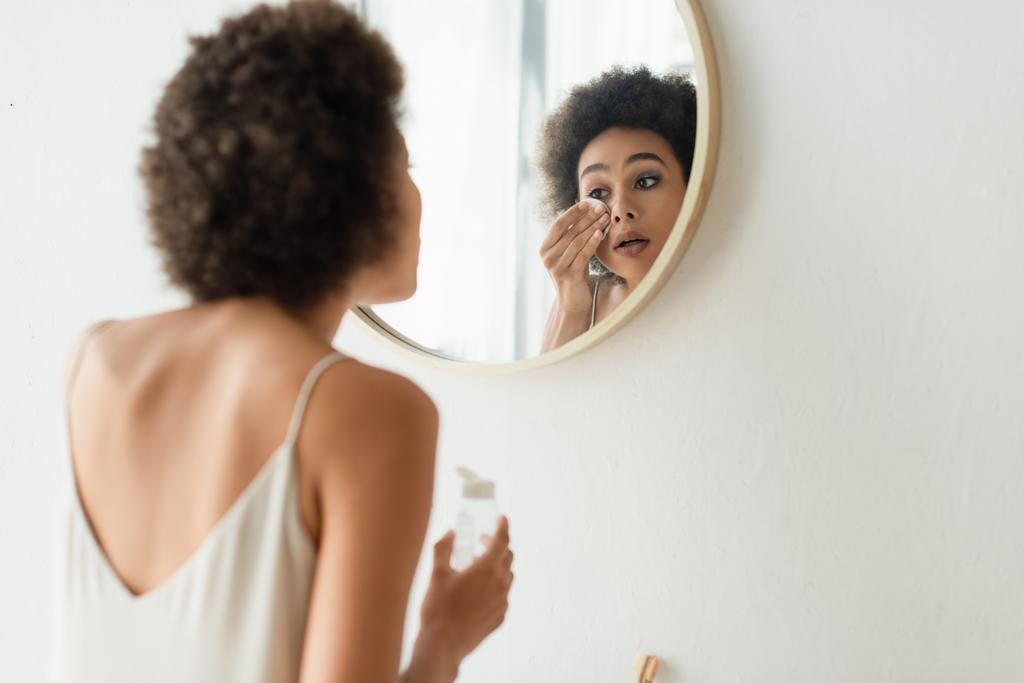 Mladá africká americká žena čištění obličeje s bavlněnou podložkou v koupelně  - Fotografie, Obrázek
