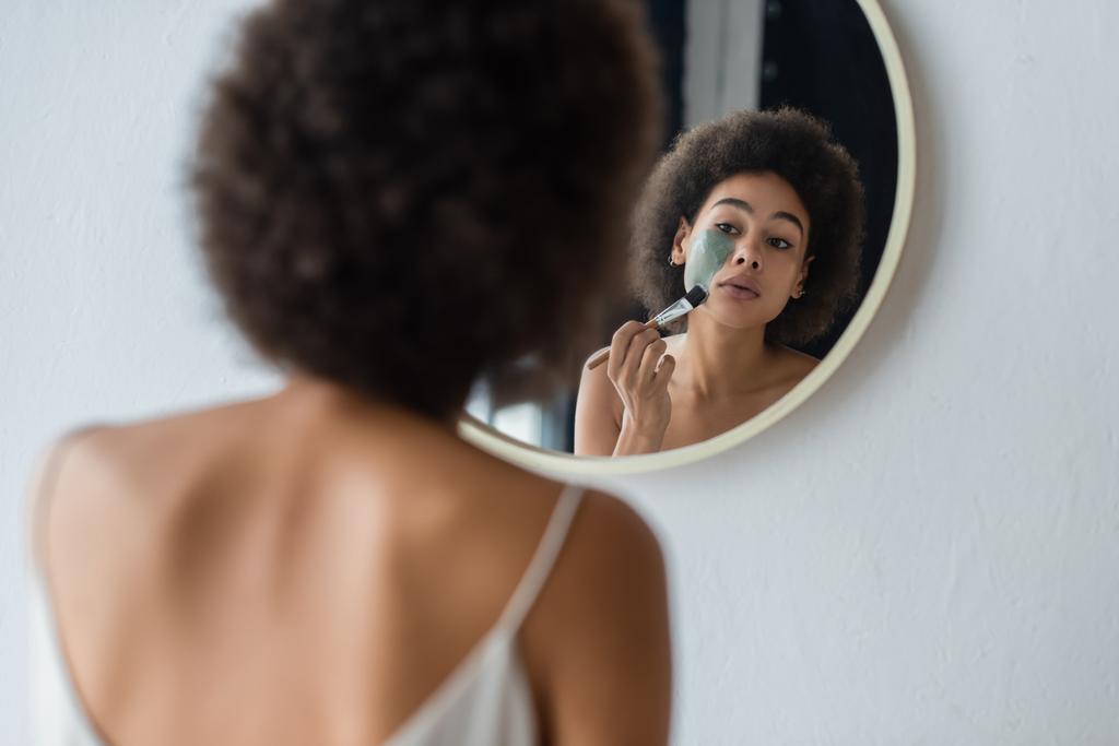 Afričanky americká žena použití tvář maska v blízkosti zrcadla v koupelně  - Fotografie, Obrázek