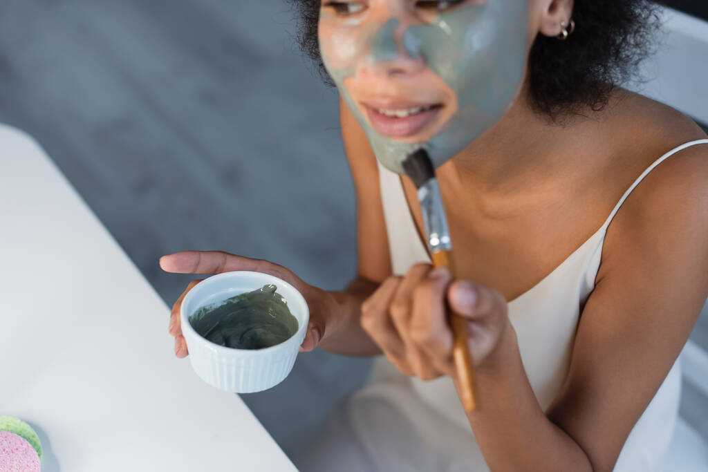 Розбитий погляд на афро - американську жінку, яка застосовує глиняну маску вдома.  - Фото, зображення