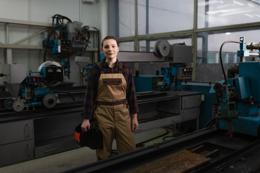 Svářečka drží svařovací masku v blízkosti strojů v továrně  - Fotografie, Obrázek