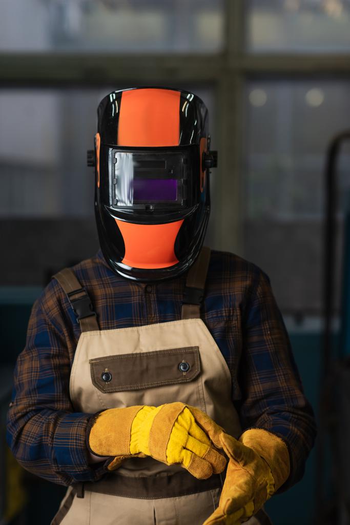 Сварщик в маске с козырьком в перчатках на заводе  - Фото, изображение