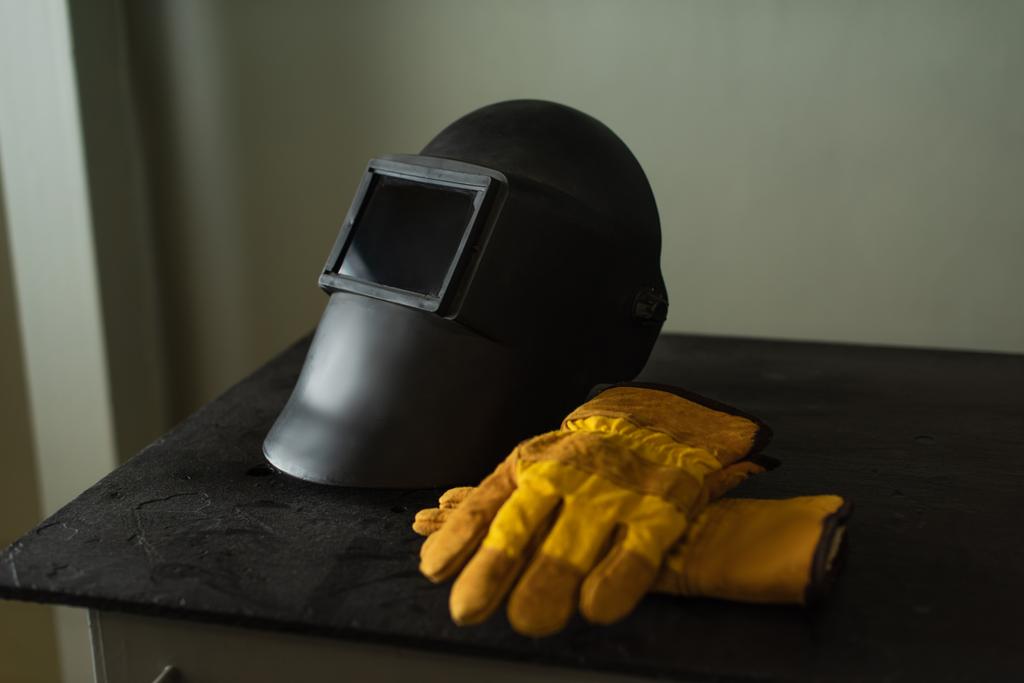 Máscara de soldadura con visera y guantes en la mesa en fábrica  - Foto, Imagen