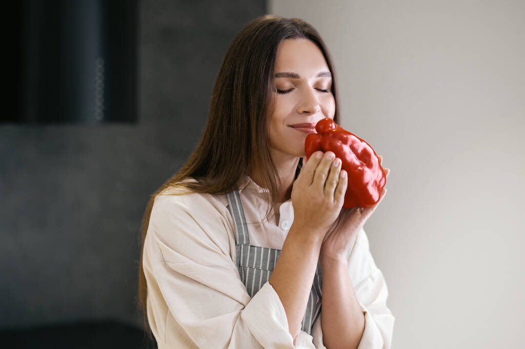 Длинноволосая молодая женщина с красным перцем в руках - Фото, изображение