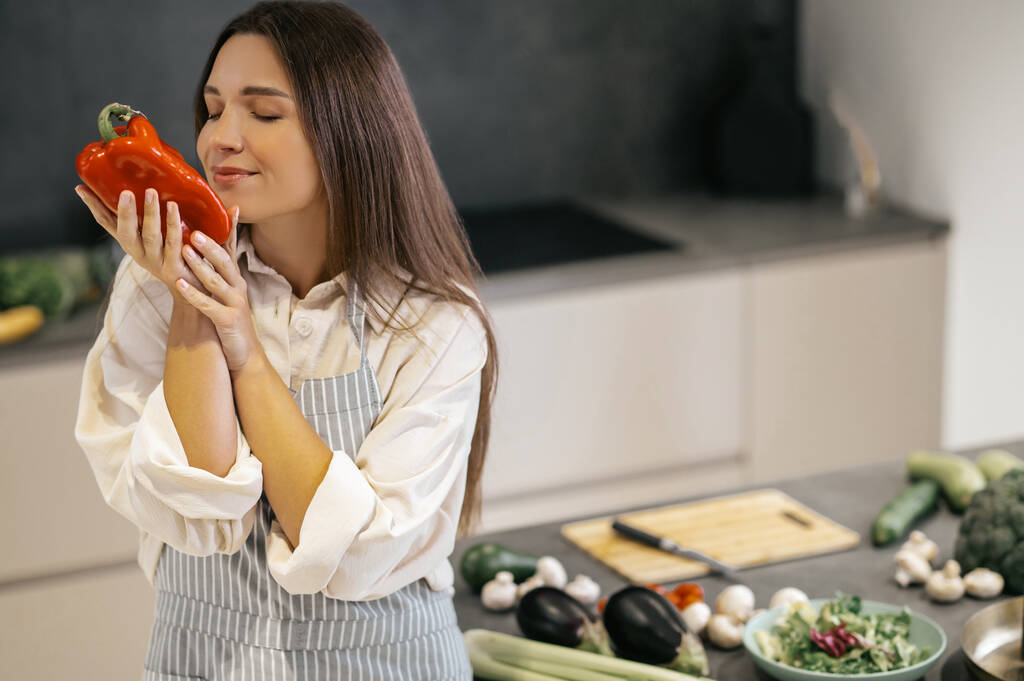 Pretty young woman smelling a red pepper with her eyes closed - Photo, Image