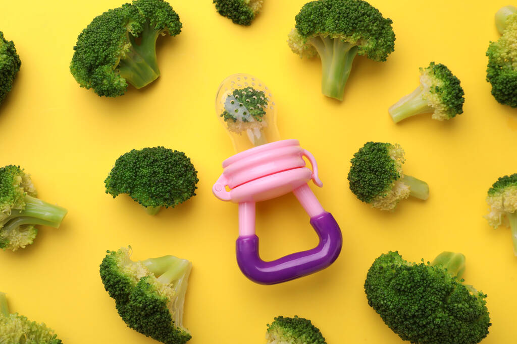 Knabbeltje met gekookte broccoli op gele ondergrond, plat gelegd. Zuigelingenvoeding - Foto, afbeelding