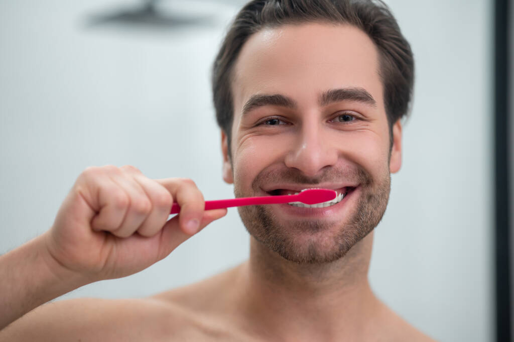 Hymyilevä nuori mies pesee hampaitaan ja näyttää huolettomalta - Valokuva, kuva