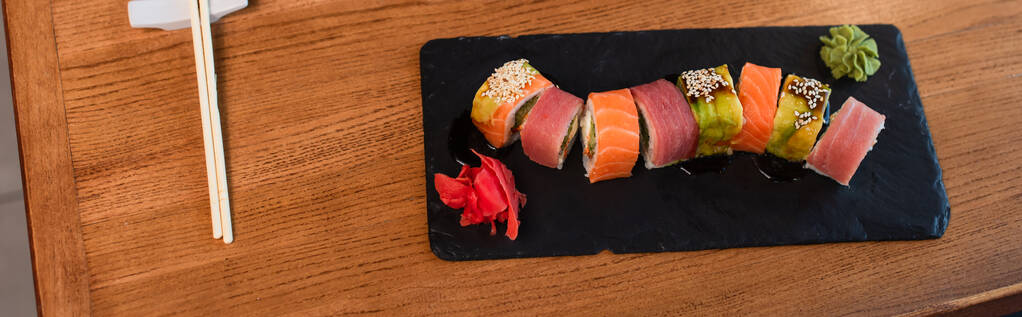 widok z góry pyszne sushi rolki z sezamem w pobliżu pałeczek na drewnianym stole, baner - Zdjęcie, obraz