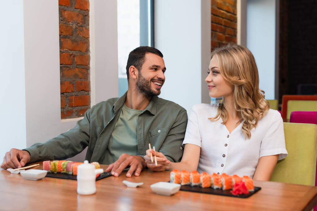 cheerful couple looking at each other during delicious dinner in sushi bar - Photo, Image
