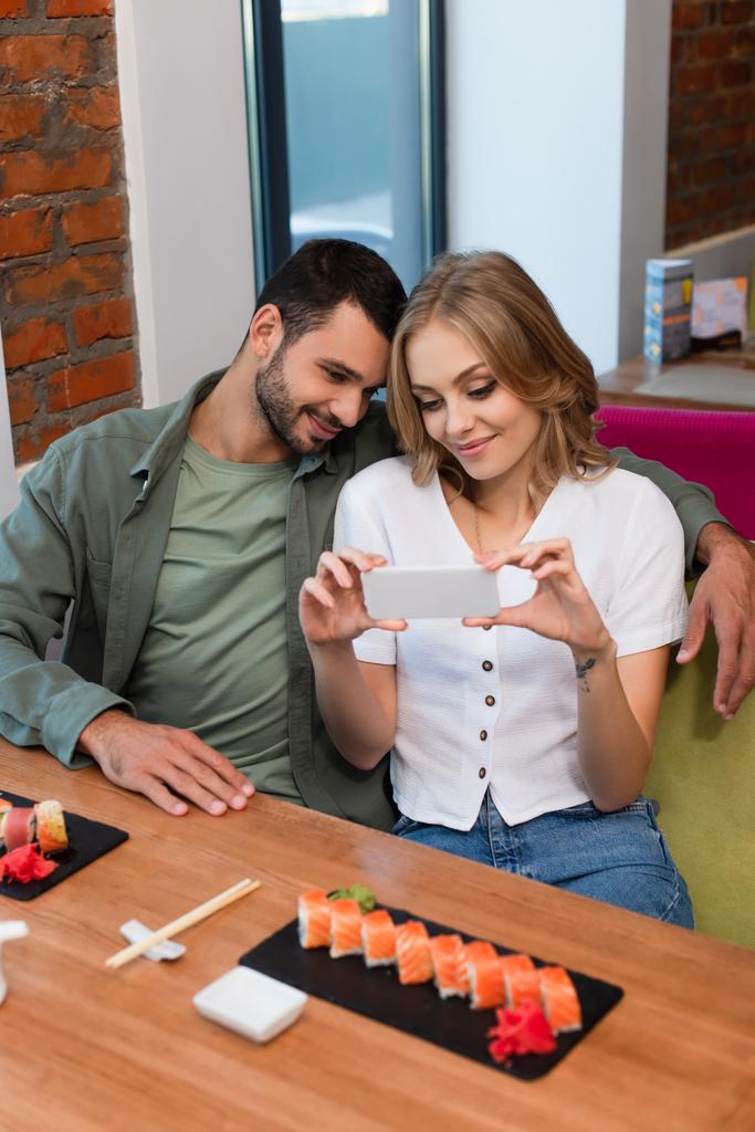 vrouw het nemen van foto van sushi rollen op smartphone in de buurt glimlachende vriendje - Foto, afbeelding
