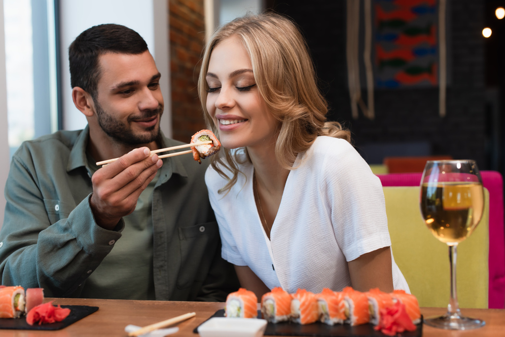 Genç adam lokantada yemek boyunca suşiyle mutlu kadını besliyor. - Fotoğraf, Görsel