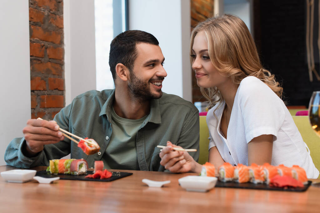 Ευτυχισμένος άντρας να μιλάει σε ξανθιά κοπέλα κατά τη διάρκεια του γεύματος στο σούσι μπαρ - Φωτογραφία, εικόνα