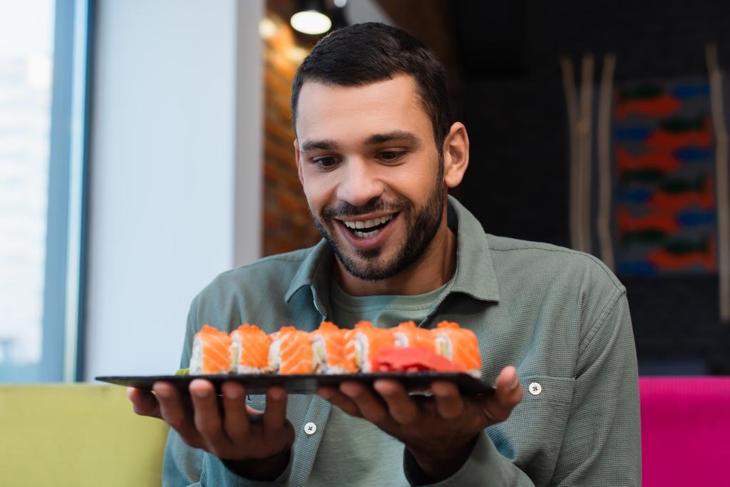 užaslý muž drží talíř s sadou chutných sushi rolky v restauraci - Fotografie, Obrázek