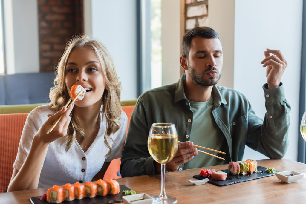 Мужчина с закрытыми глазами наслаждается вкусными суши возле улыбающейся девушки  - Фото, изображение