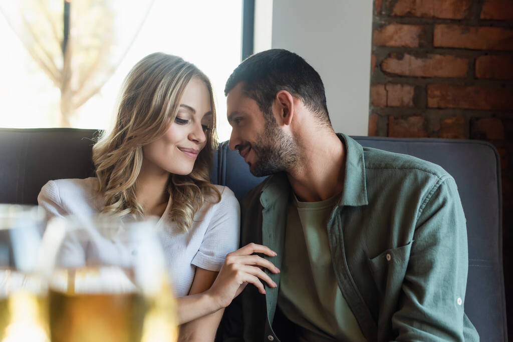 young couple smiling during date in restaurant near wine glasses on blurred foreground - Foto, Bild