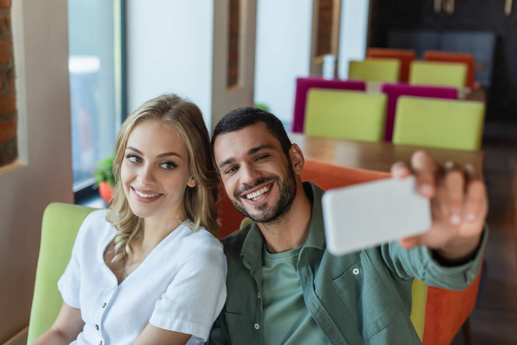 cheerful couple taking selfie on blurred mobile phone in cafe - Photo, Image