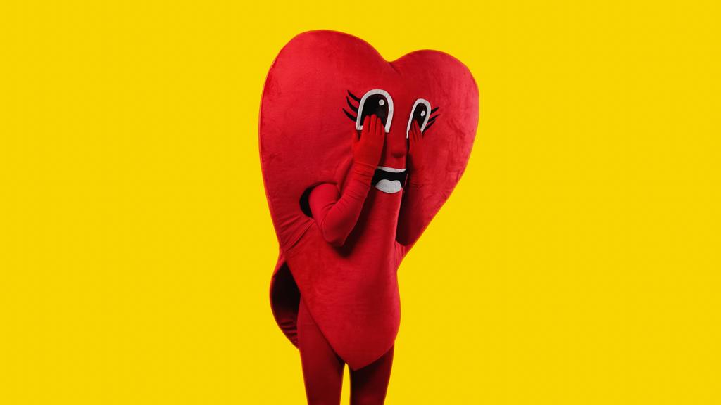 pessoa triste no traje do coração tocando os olhos dos desenhos animados enquanto imita choro isolado no amarelo - Foto, Imagem