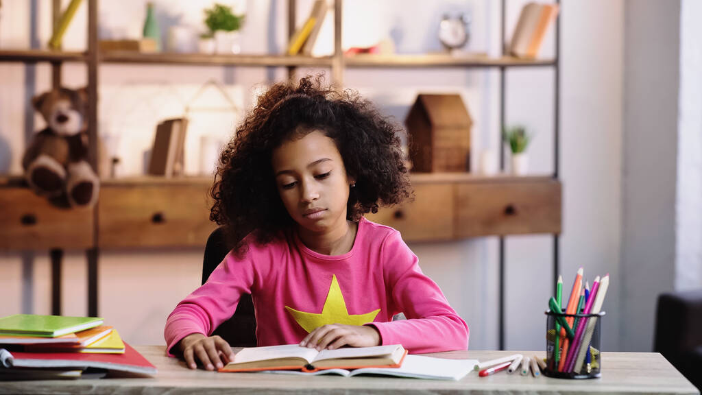 кучерявий афроамериканський школяр читає книгу вдома
  - Фото, зображення