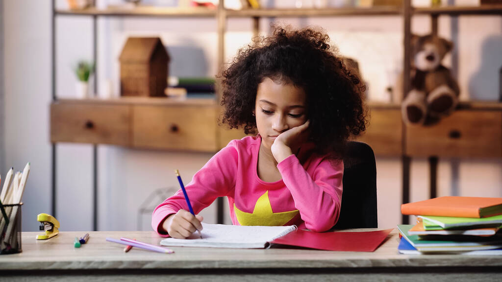 ennuyé afro-américaine fille écrit dans un carnet tout en faisant des devoirs - Photo, image