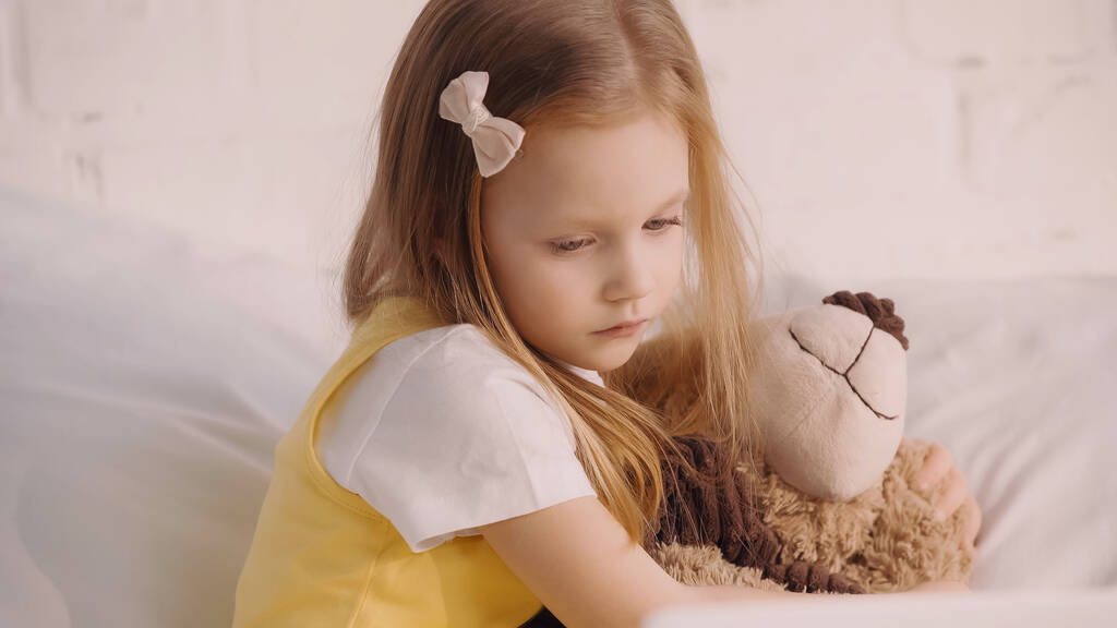Παιδί αγκαλιάζει αρκουδάκι στο κρεβάτι στο σπίτι  - Φωτογραφία, εικόνα