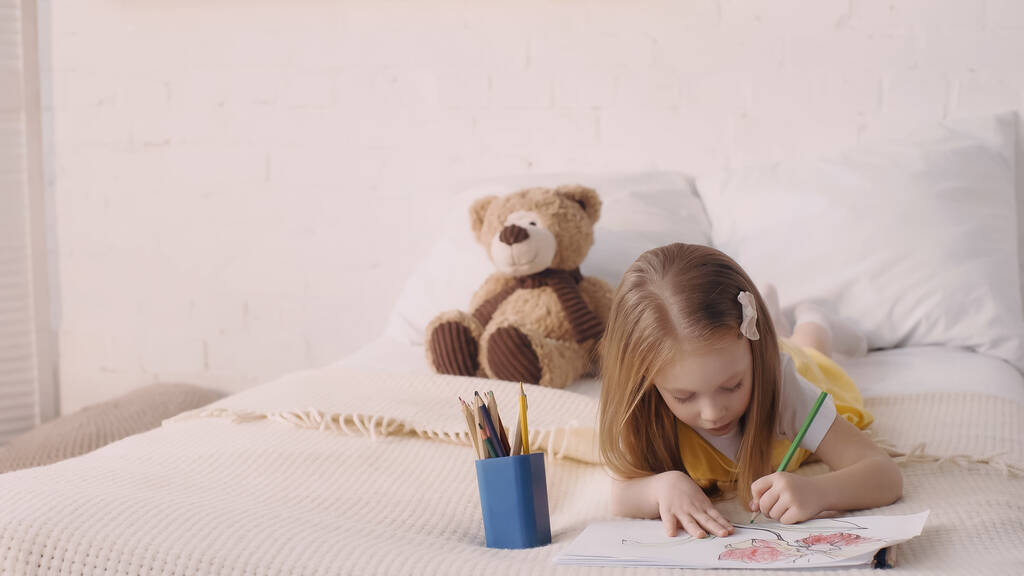 Chica dibujo sobre papel cerca de lápices de color en el dormitorio  - Foto, imagen