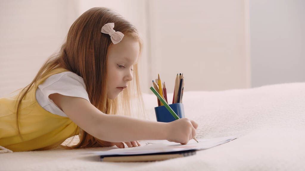 Kid drawing on paper while lying on blanket on bed  - Photo, Image