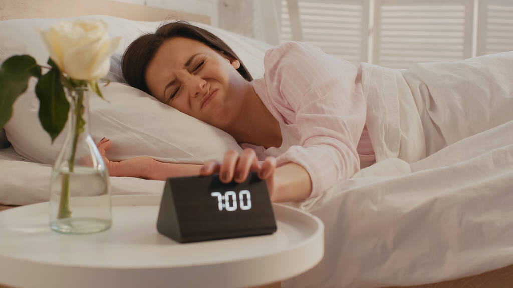 Displeased woman turning off clock near flower in bedroom at home  - Foto, Imagem