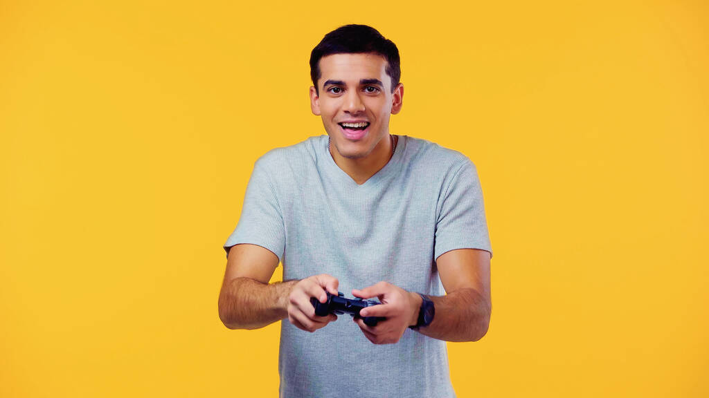 QUIIV, UCRÂNIA - 22 DE DEZEMBRO DE 2021: jovem animado segurando joystick e jogando videogame isolado em amarelo - Foto, Imagem