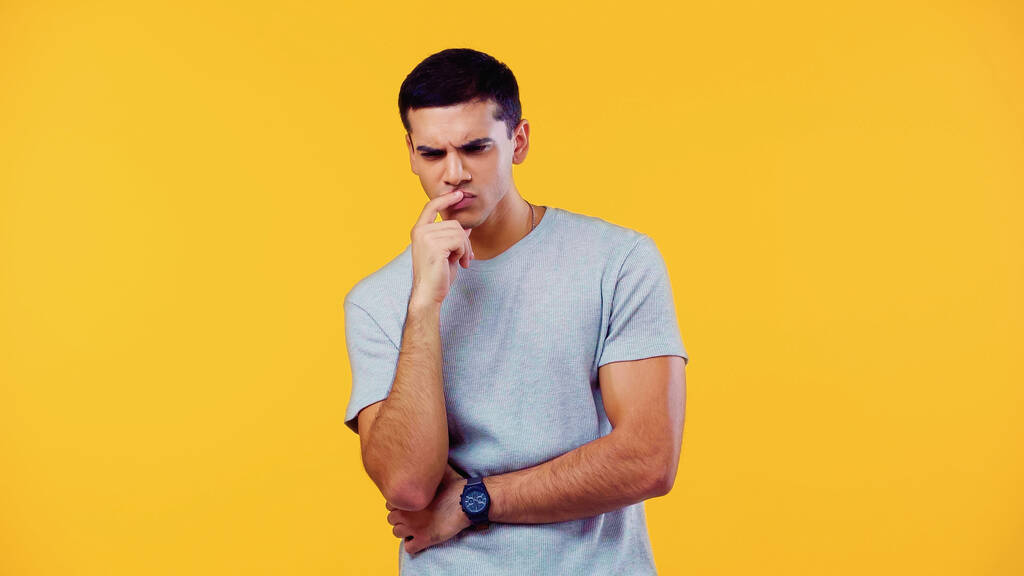 pensive young man in t-shirt touching lips isolated on yellow - Foto, Bild
