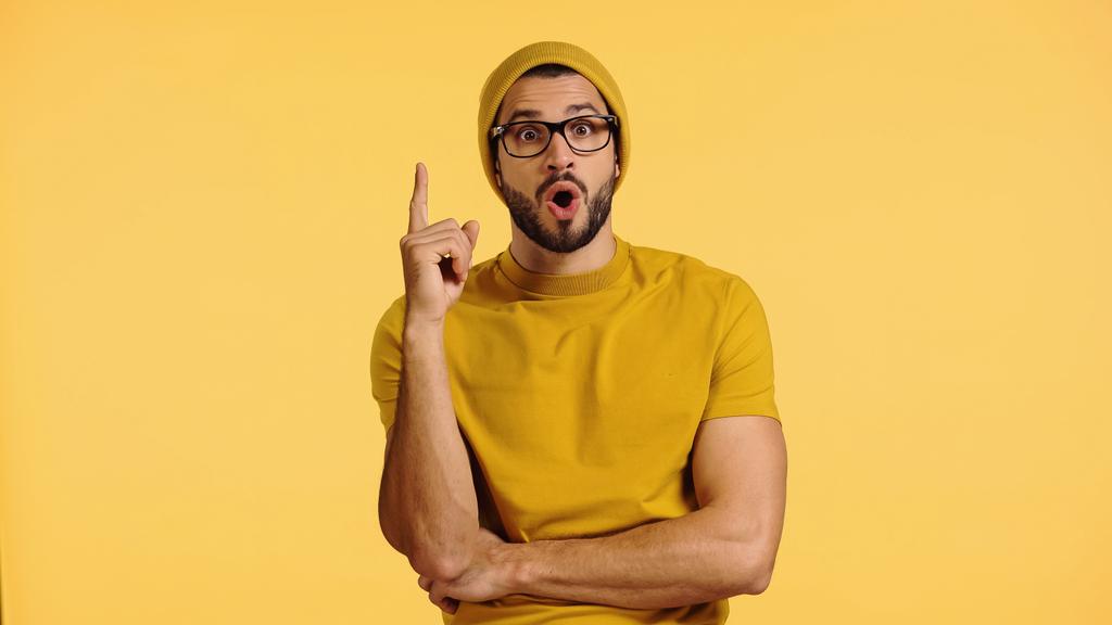 surprised young man in beanie hat showing idea sign isolated on yellow  - Фото, изображение