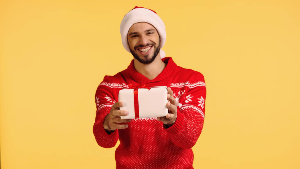 happy man in santa hat holding gift box isolated on yellow - Фото, изображение