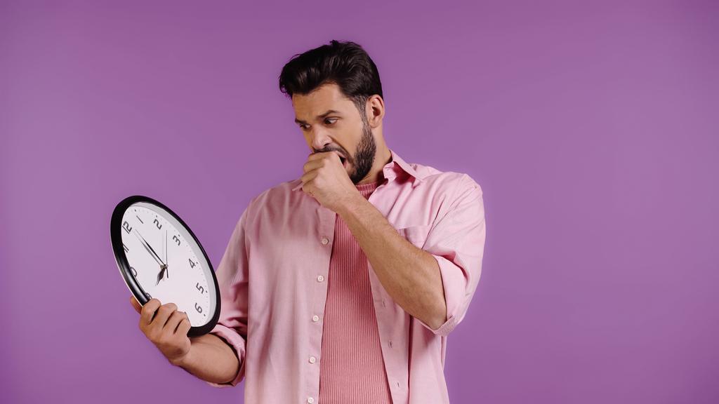worried young man looking at clock isolated on purple  - Foto, Imagem