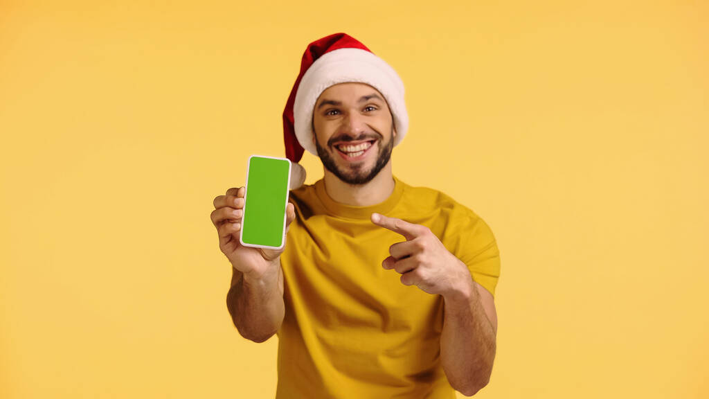 uomo allegro in cappello di Babbo Natale che punta a smartphone con schermo verde isolato su giallo - Foto, immagini