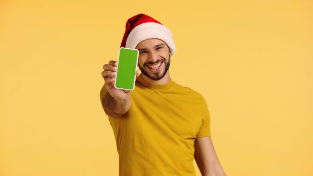 homem satisfeito em santa chapéu segurando smartphone com tela verde isolada no amarelo - Foto, Imagem